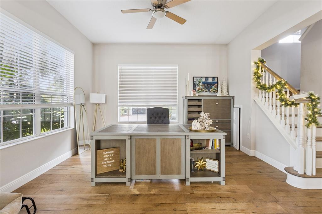A home office features a large wooden desk, hardwood floors, and a staircase with garland — 3443 TUMBLING RIVER DRIVE, CLERMONT, FL