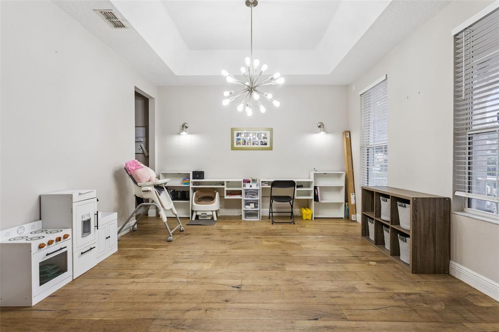 A playroom features wood-look flooring, a white desk unit, a toy kitchen, and a chandelier — 3443 TUMBLING RIVER DRIVE, CLERMONT, FL