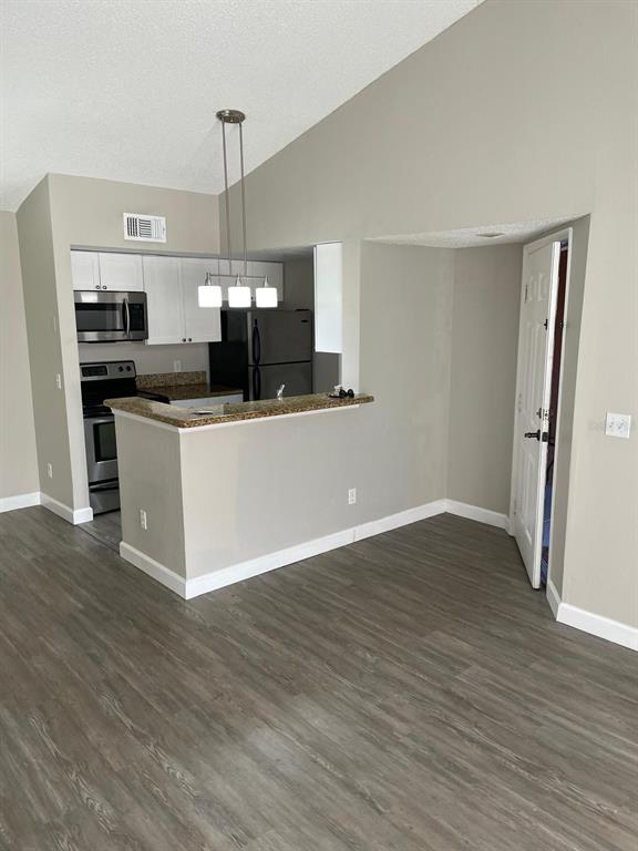 A kitchen with white cabinets and stainless steel appliances overlooks a living area with flooring — 5140 CONROY ROAD UNIT 35, ORLANDO, FL