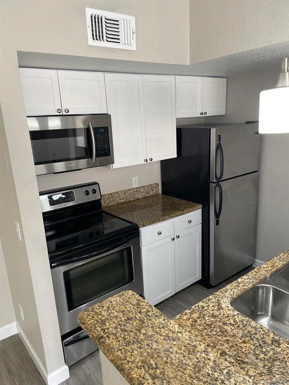 A kitchen features white cabinets, stainless steel appliances, and speckled granite countertops — 5140 CONROY ROAD UNIT 35, ORLANDO, FL