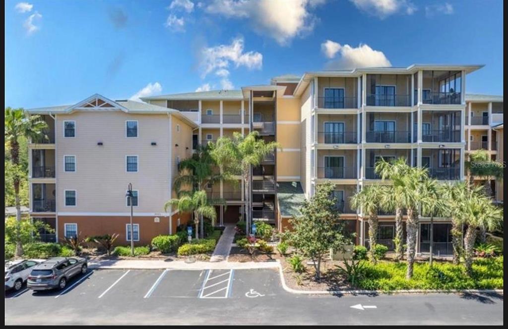 A multi-story apartment building with tan siding, screened balconies, and a paved parking lot — 9051 TREASURE TROVE LANE UNIT 505, KISSIMMEE, FL