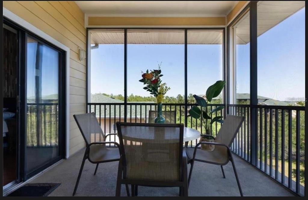 A screened-in balcony features a dining set, potted plants, and views of surrounding trees — 9051 TREASURE TROVE LANE UNIT 505, KISSIMMEE, FL