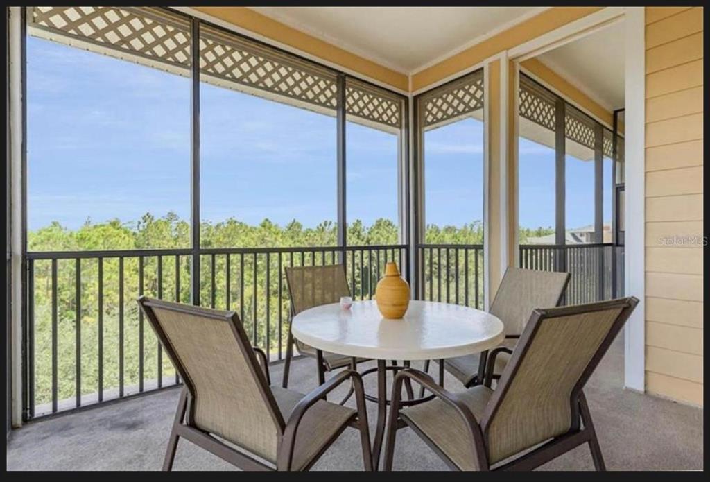 A screened-in balcony features a round table with four chairs overlooking a wooded area — 9051 TREASURE TROVE LANE UNIT 505, KISSIMMEE, FL