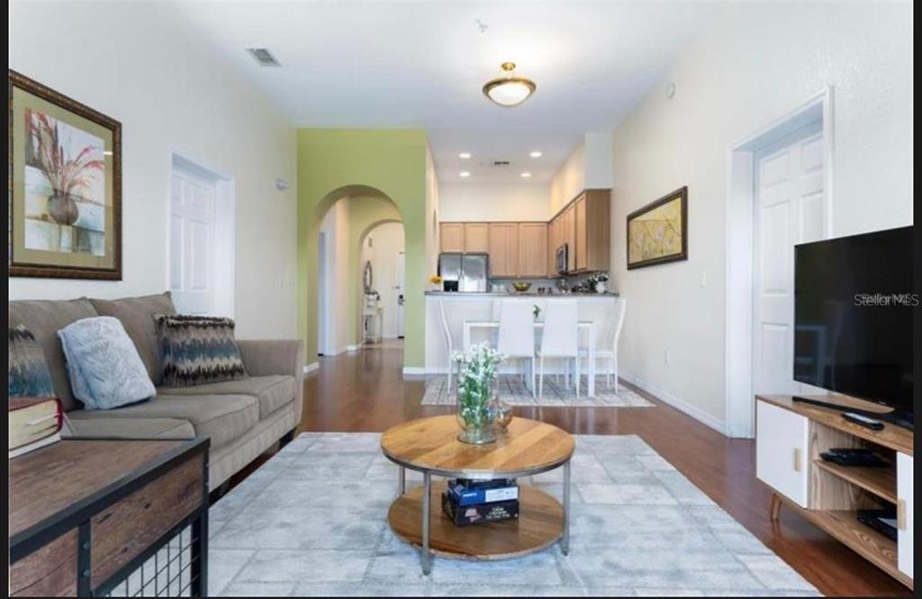 A living room with a sofa, coffee table, and television leads into an open-concept kitchen — 9051 TREASURE TROVE LANE UNIT 505, KISSIMMEE, FL