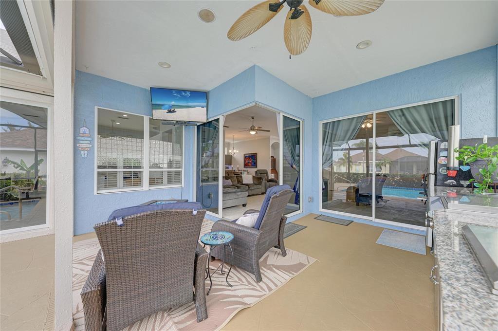 A covered patio features blue walls, wicker furniture, a ceiling fan, and sliding glass doors — 4735 SPINNAKER DRIVE, BRADENTON, FL