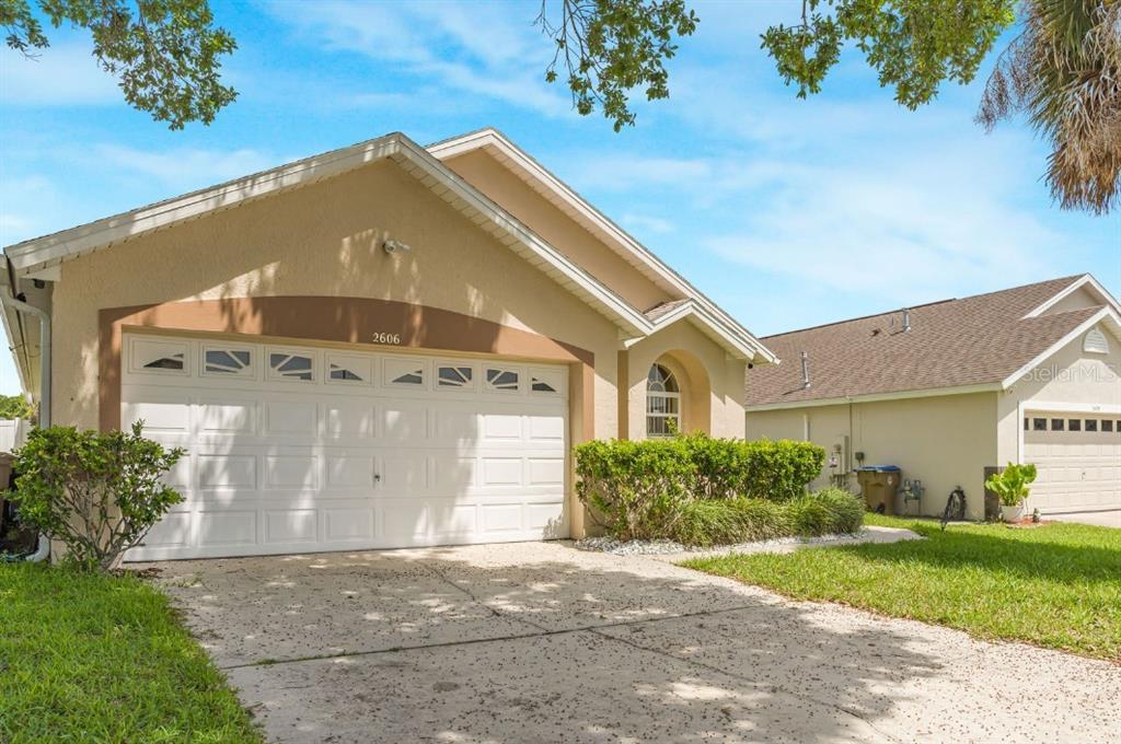 A tan single-story house with a white two-car garage and a concrete driveway — 2606 LUISENO WAY, KISSIMMEE, FL
