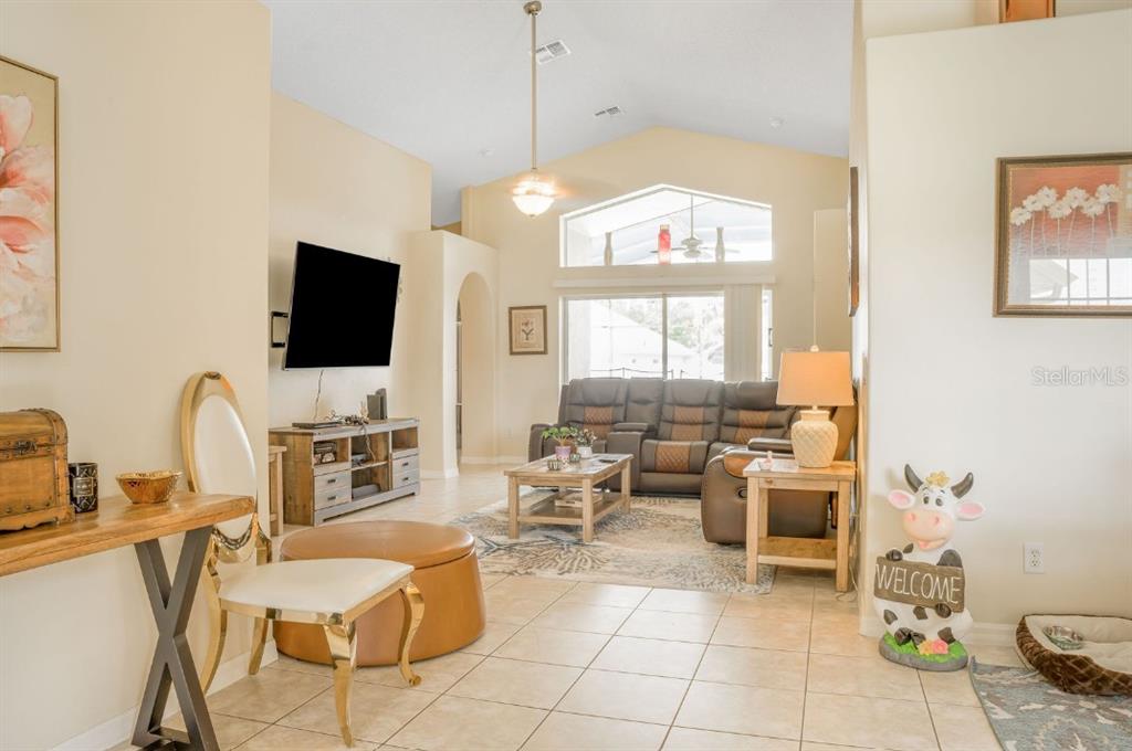 A living room features vaulted ceilings, tile flooring, a brown sectional sofa, and a television — 2606 LUISENO WAY, KISSIMMEE, FL