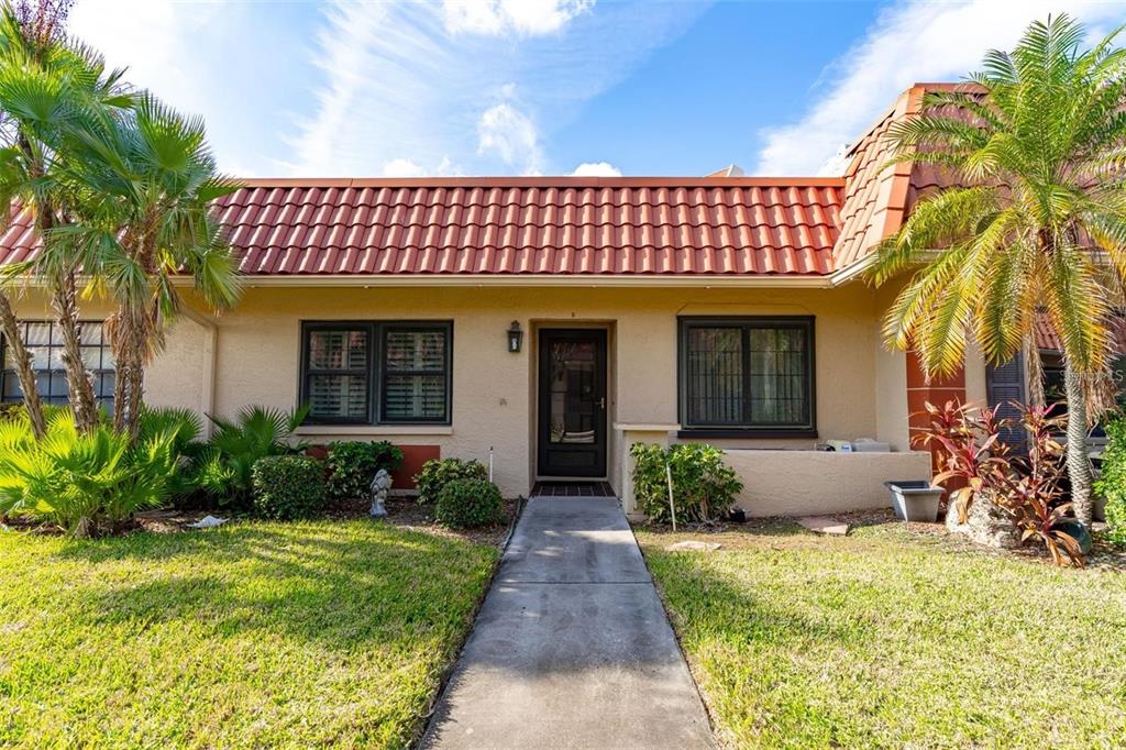 A single-story house with a red tile roof, beige stucco walls, and a concrete walkway — 19029 US HIGHWAY 19 UNIT 25D, CLEARWATER, FL