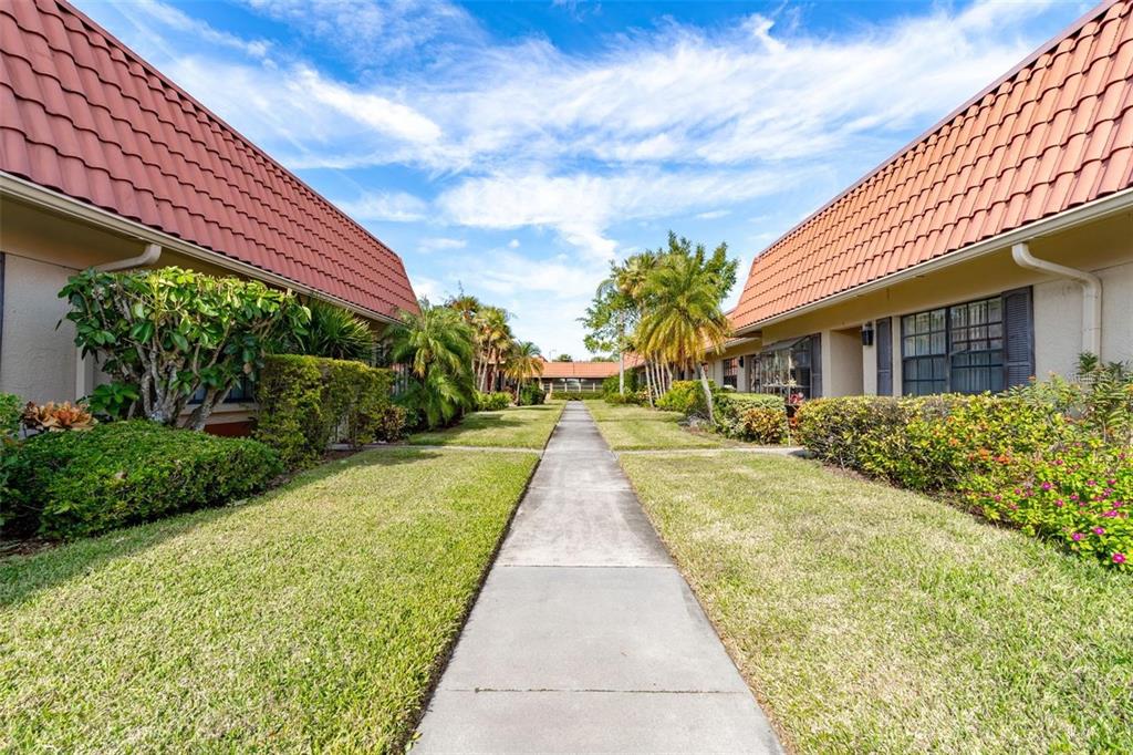 A concrete walkway leads between two single-story residential buildings with red tile roofs and landscaping — 19029 US HIGHWAY 19 UNIT 25D, CLEARWATER, FL
