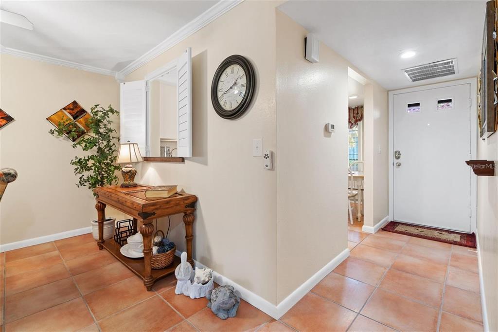 An entryway features tiled floors, a wooden console table, a wall clock, and a white door — 19029 US HIGHWAY 19 UNIT 25D, CLEARWATER, FL