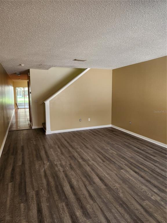 An empty living room features wood-look flooring, tan walls, and a staircase with white trim — 10815 BRICKSIDE COURT, RIVERVIEW, FL