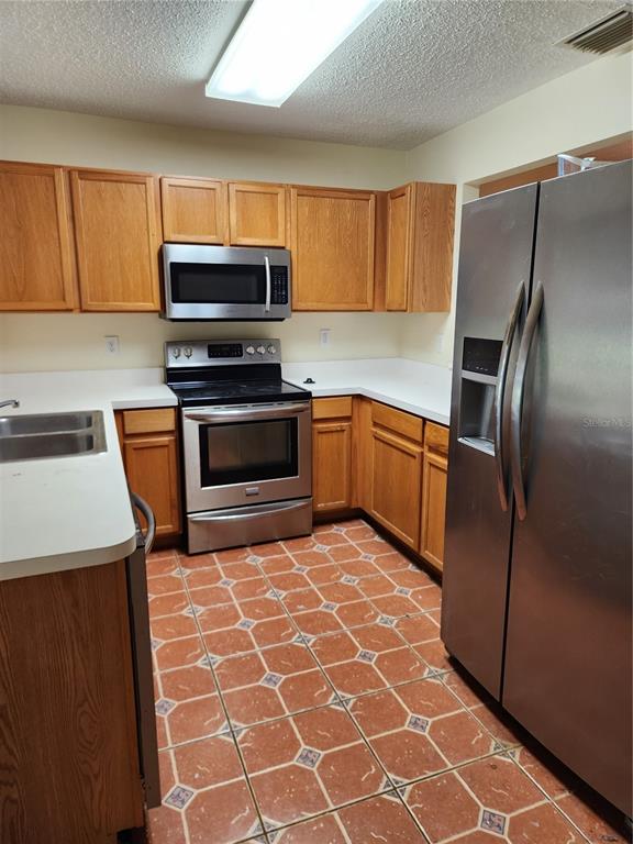 A kitchen features oak cabinets, stainless steel appliances, white countertops, and patterned tile flooring — 10815 BRICKSIDE COURT, RIVERVIEW, FL