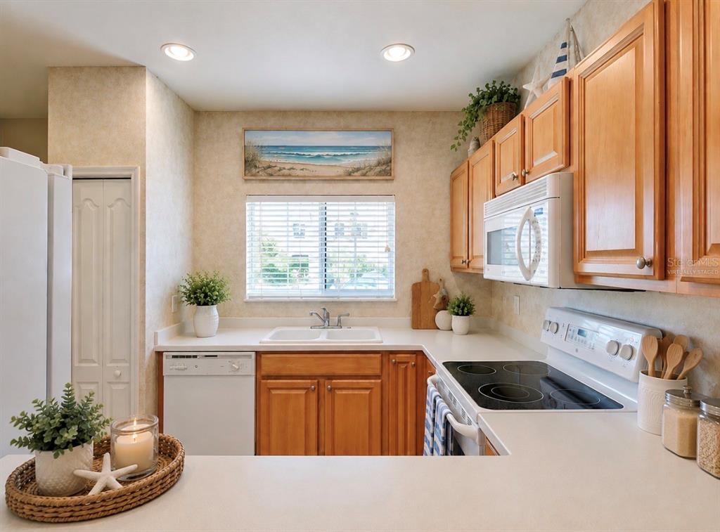 A kitchen features light wood cabinets, white appliances, a window above the sink, and countertops — 13050 TIGERS EYE DRIVE, VENICE, FL