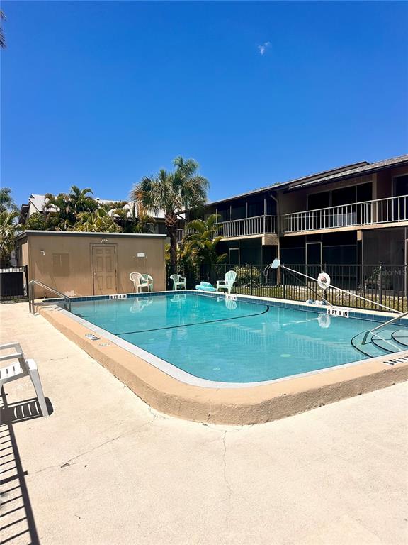 A rectangular swimming pool sits in front of a tan utility building and apartment complex — 2938 CLARK ROAD UNIT 102, SARASOTA, FL