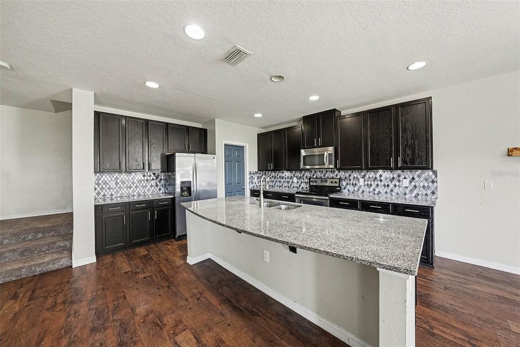 A kitchen features dark wood cabinets, granite countertops, a large island, and wood-look flooring — 10233 NEWMINSTER LOOP, RUSKIN, FL