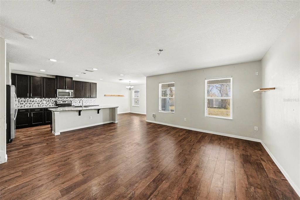 An open-concept kitchen and living area featuring dark wood cabinets, a breakfast bar, and flooring — 10233 NEWMINSTER LOOP, RUSKIN, FL