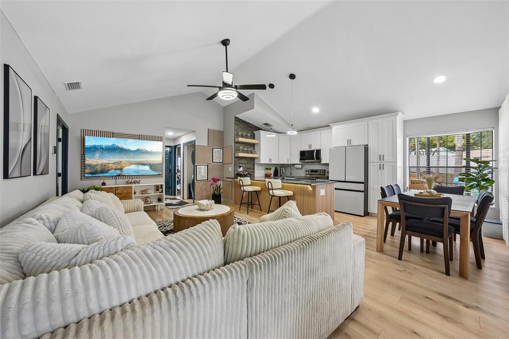An open-concept living room and kitchen featuring a sectional sofa, dining area, and white cabinetry — 3376 SHORNCLIFFE LANE, PALM HARBOR, FL