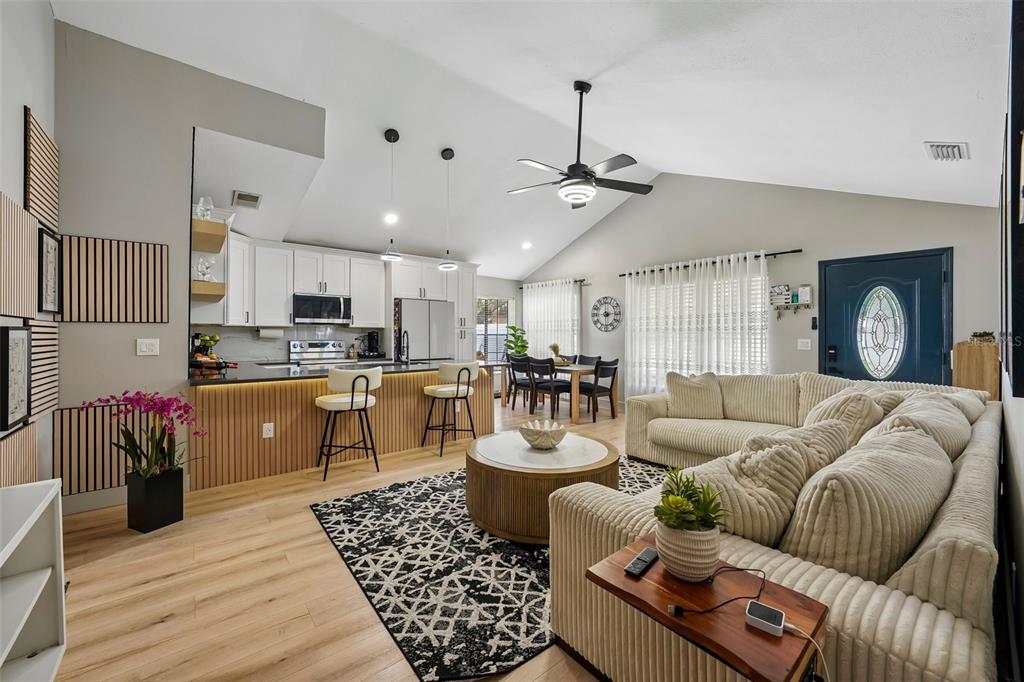 An open-concept living room and kitchen featuring light wood floors, white cabinetry, and vaulted ceilings — 3376 SHORNCLIFFE LANE, PALM HARBOR, FL