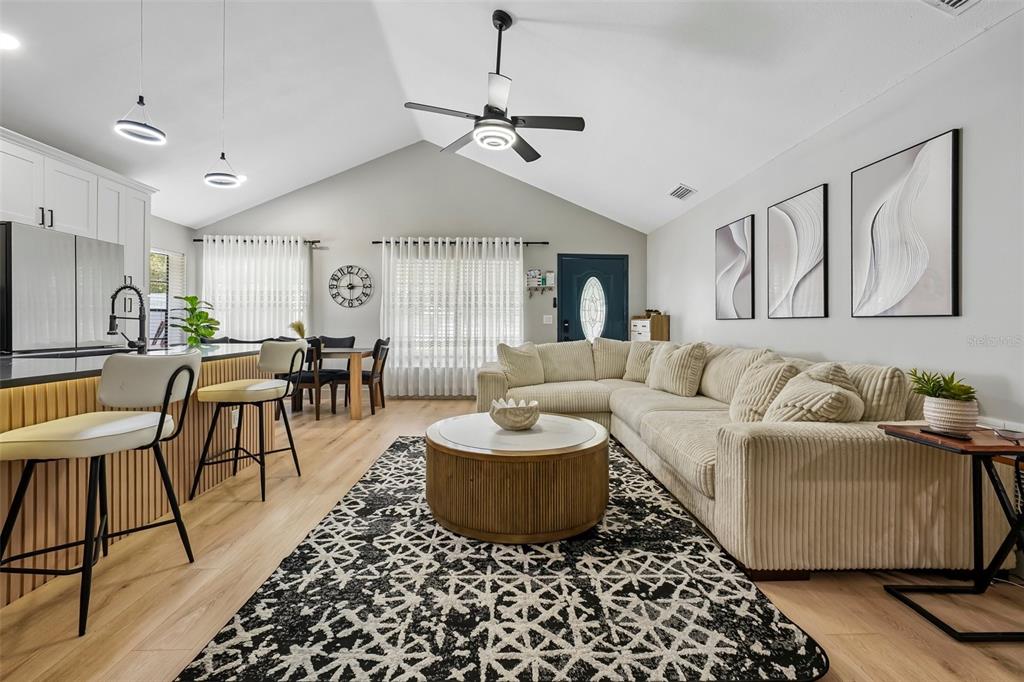 A living room with a vaulted ceiling, sectional sofa, round coffee table, and kitchen island — 3376 SHORNCLIFFE LANE, PALM HARBOR, FL