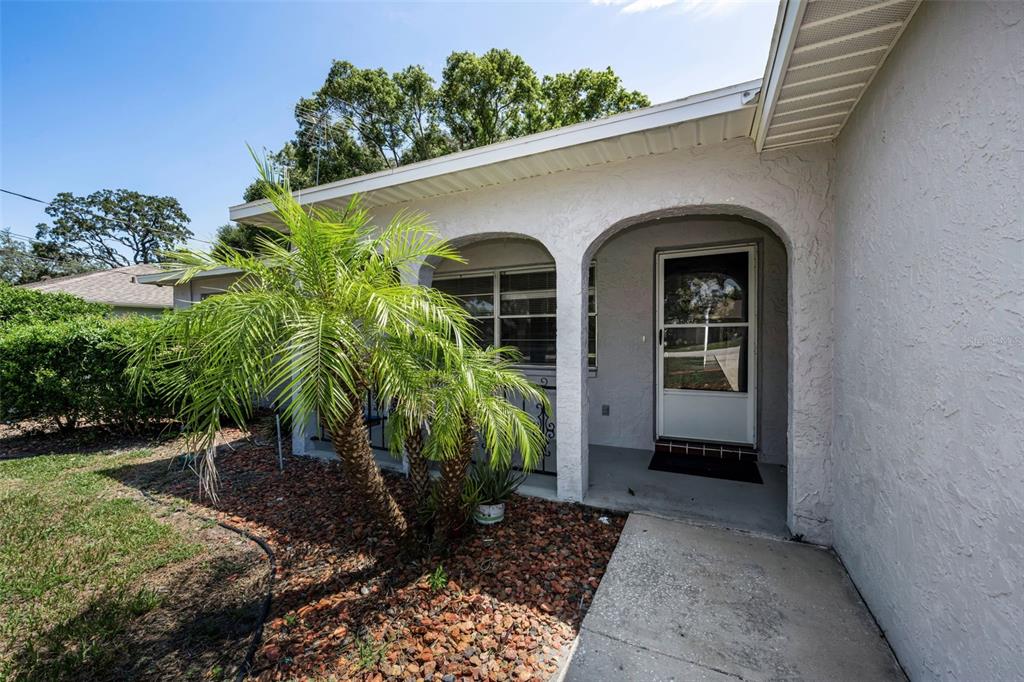 A palm tree sits in a rock garden beside the arched entryway of a house — 362 PORTLAND AVENUE, SPRING HILL, FL