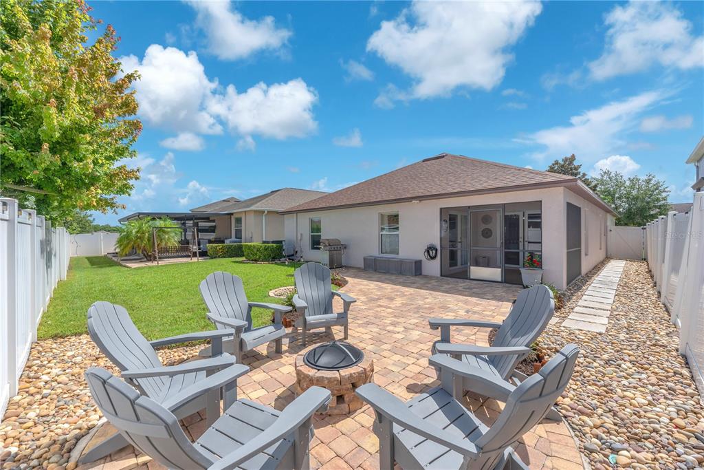A backyard patio features a stone fire pit surrounded by gray Adirondack chairs — 10904 RAINBOW PYRITE DRIVE, WIMAUMA, FL