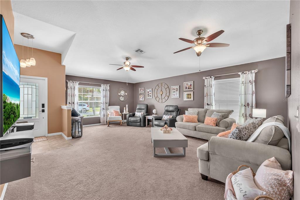 A spacious living room features carpeted floors, two ceiling fans, and neutral-toned walls — 10904 RAINBOW PYRITE DRIVE, WIMAUMA, FL
