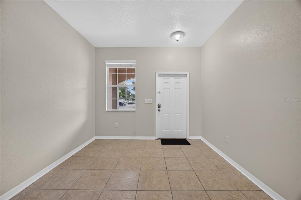An empty room features beige walls, a tiled floor, a window, and a white front door — 10709 SAVANNAH LANDING CIRCLE, ORLANDO, FL