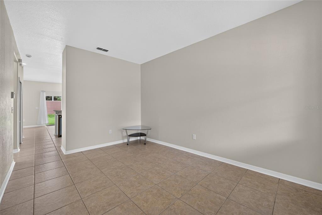 An empty room with beige walls and light brown tile flooring features a glass side table — 10709 SAVANNAH LANDING CIRCLE, ORLANDO, FL