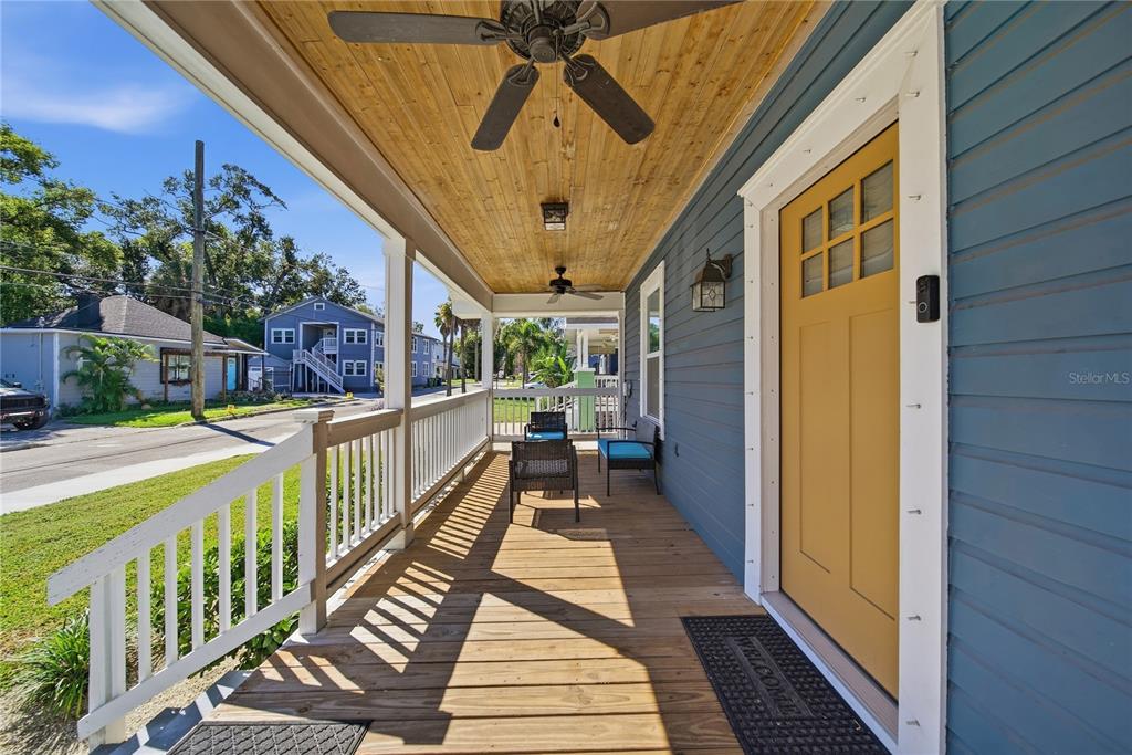 A wooden front porch with a yellow door, ceiling fans, and outdoor seating — 2910 N OLA AVENUE, TAMPA, FL