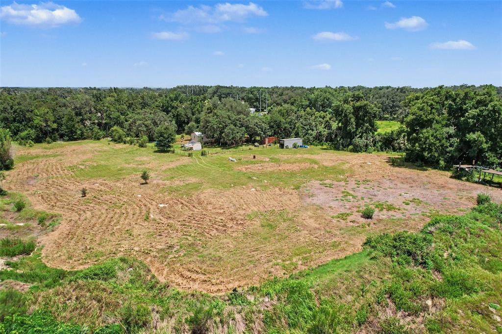 An aerial view shows a large, cleared grassy lot surrounded by dense trees and vegetation — 10239 LYONS AVENUE, LITHIA, FL