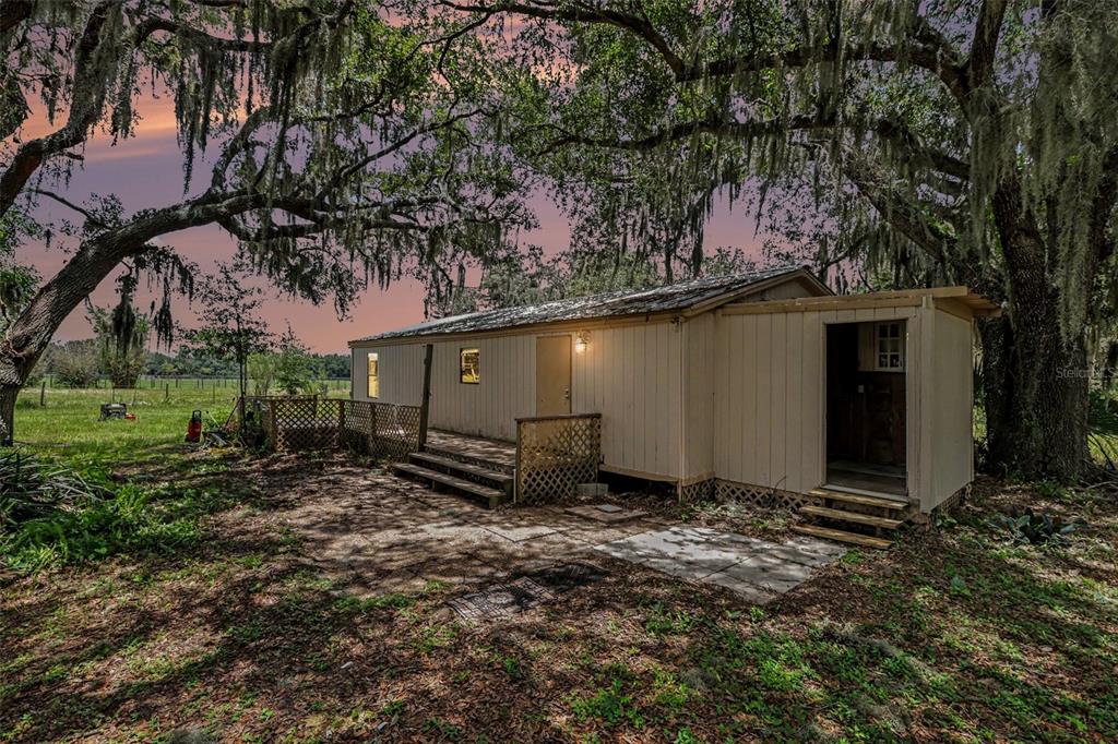 A single-story mobile home with a wooden deck sits under large oak trees at dusk — 10239 LYONS AVENUE, LITHIA, FL