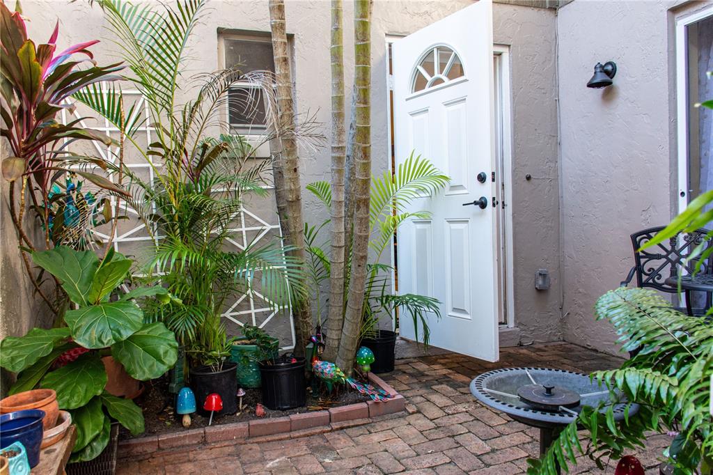 A small brick patio features potted plants, a birdbath, and an open white door — 155 FALLWOOD STREET, FERN PARK, FL
