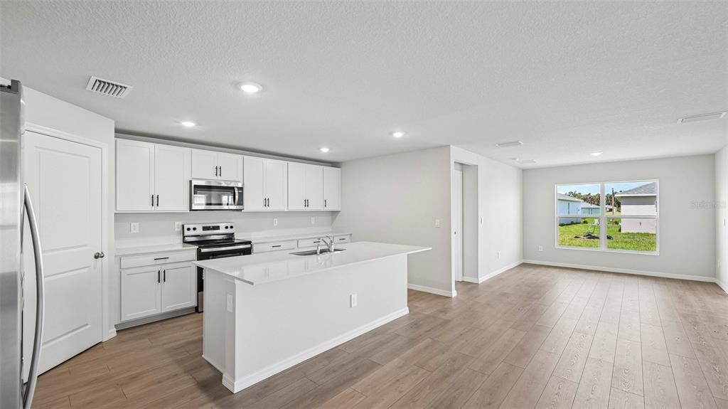 A modern kitchen features white cabinets, stainless steel appliances, and a large island with sink — 17616 WHISKEY CREEK TRAIL, PARRISH, FL