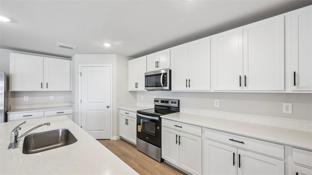 A kitchen features white cabinets, stainless steel appliances, and a white quartz island countertop — 17616 WHISKEY CREEK TRAIL, PARRISH, FL