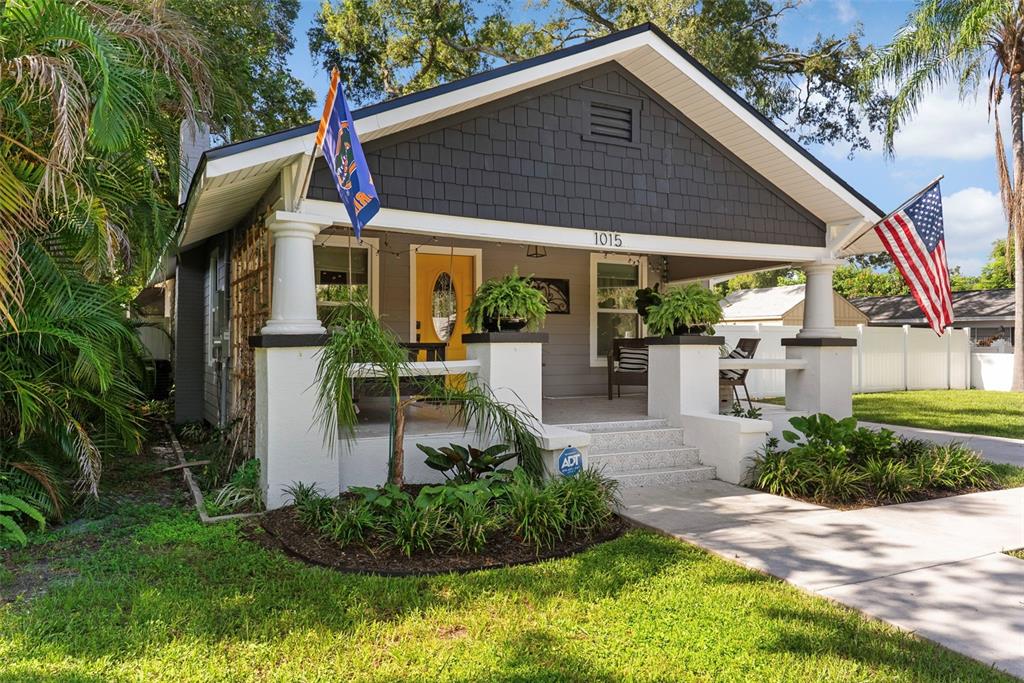 A gray bungalow with a yellow front door, a covered porch, and two flags — 1015 E CRAWFORD STREET, TAMPA, FL
