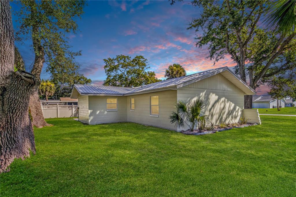 A light-colored, single-story house with a metal roof sits on a grassy lawn — 5464 RIVERSIDE DRIVE, PORT ORANGE, FL