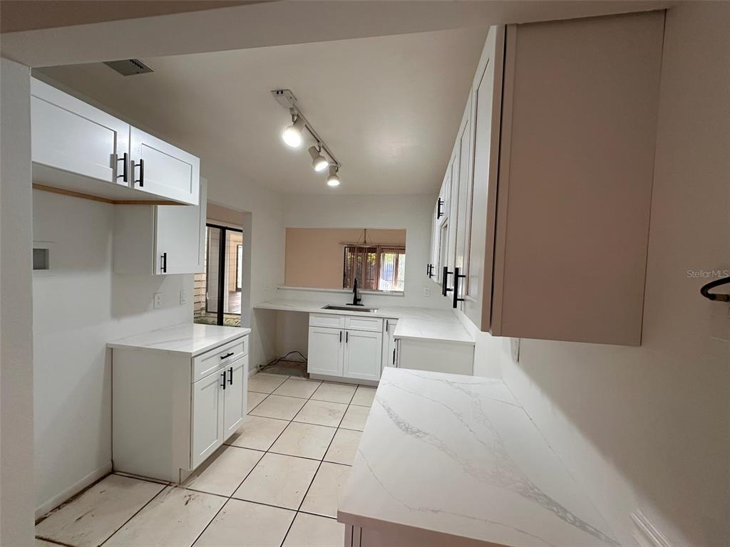 A kitchen features white cabinets, marble-look countertops, and tile flooring under track lighting — 705 TEAL LANE, ALTAMONTE SPRINGS, FL