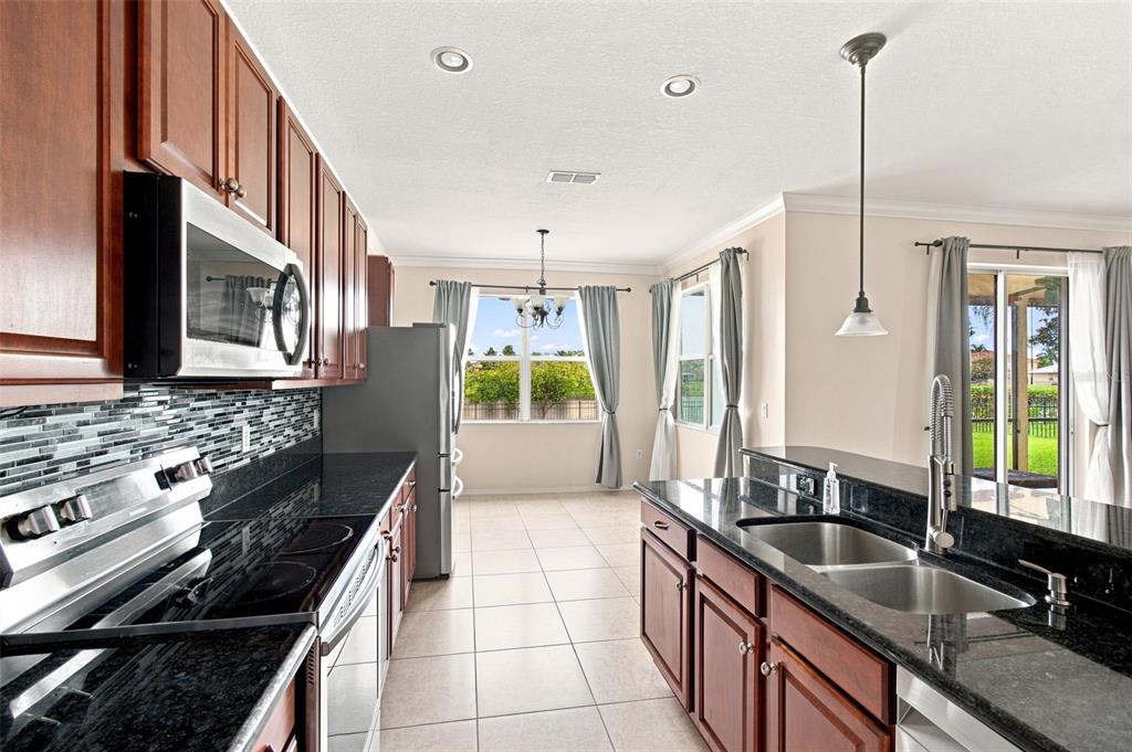 A kitchen with dark wood cabinets, black granite countertops, stainless steel appliances, and tile flooring — 5108 BUTTERFLY SHELL DRIVE, APOLLO BEACH, FL