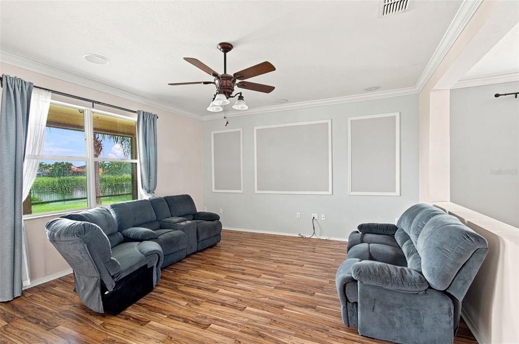 A living room with wood-look flooring, blue reclining sofas, a ceiling fan, and wall molding — 5108 BUTTERFLY SHELL DRIVE, APOLLO BEACH, FL