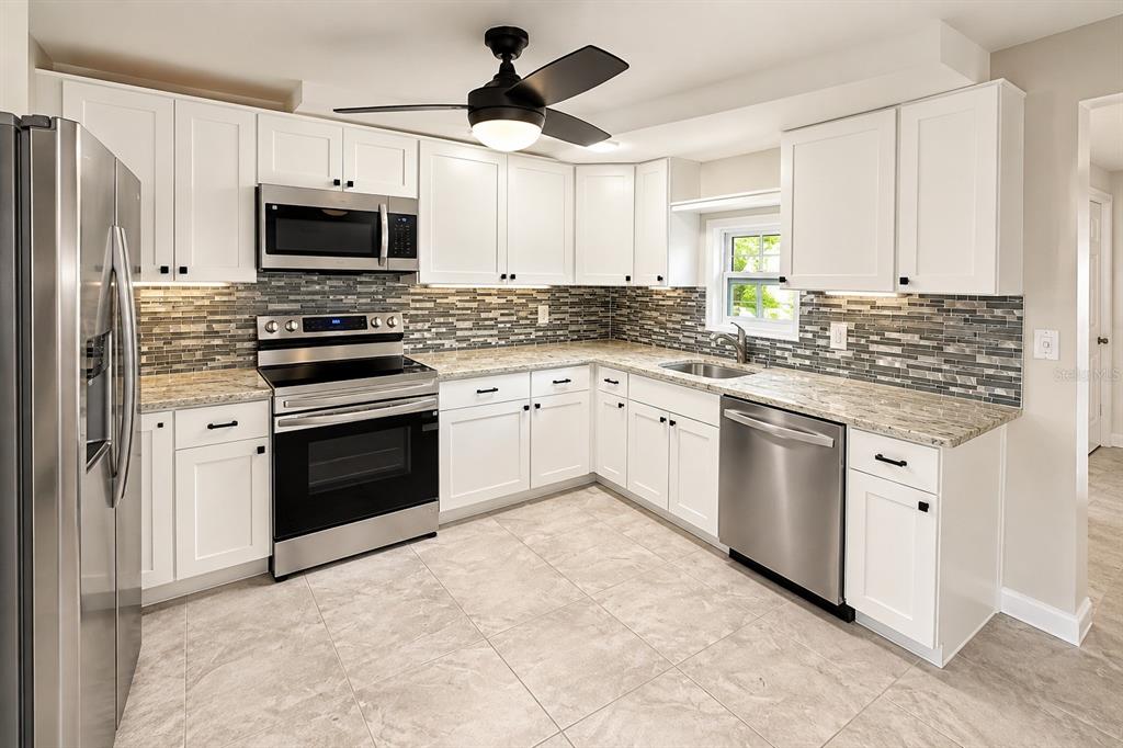 A backyard features a white house with a screened porch, landscaping, and a white fence — 4033 NEWCASTLE DRIVE, NEW PORT RICHEY, FL