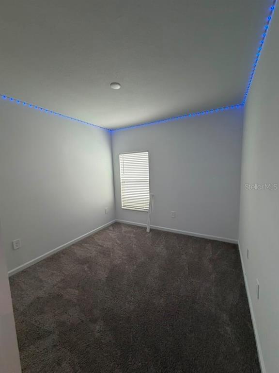 An empty bedroom features gray carpeting, white walls, and blue LED strip lighting along the ceiling — 1406 DEEPWATER CIRCLE, EAGLE LAKE, FL