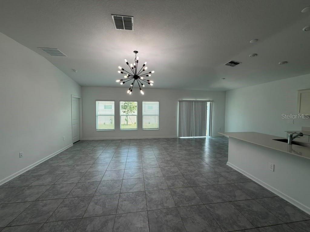 A spacious, open-concept living area with gray tile flooring, a modern chandelier, and sliding doors — 1406 DEEPWATER CIRCLE, EAGLE LAKE, FL