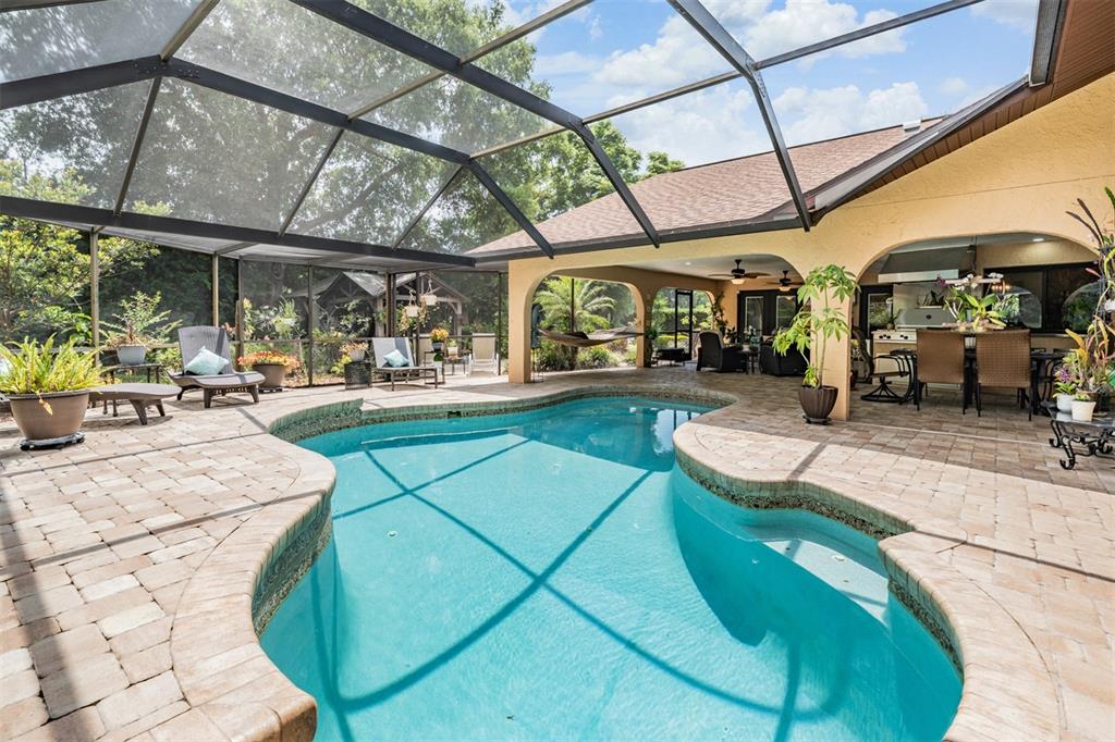 A screened-in patio features a curved swimming pool, paver decking, and an outdoor kitchen area — 13203 SPINDLEWYCK COVE, RIVERVIEW, FL