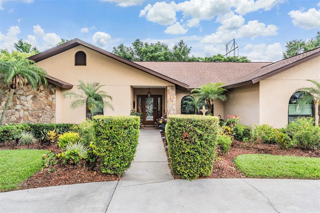 A single-story house with a tan stucco exterior, stone accents, and a front walkway — 13203 SPINDLEWYCK COVE, RIVERVIEW, FL