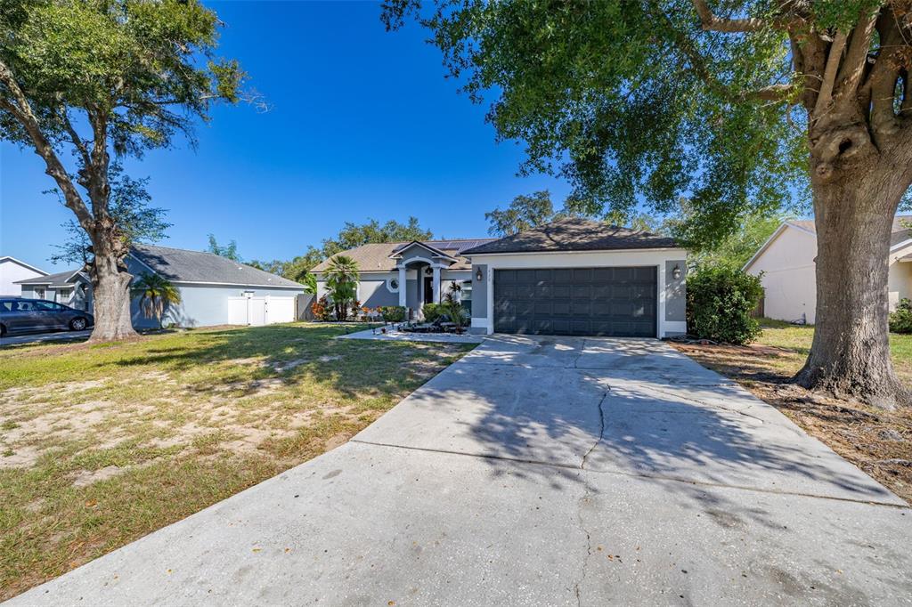 A single-story house with a gray garage, a concrete driveway, and large oak trees — 428 BENT OAK LOOP, DAVENPORT, FL