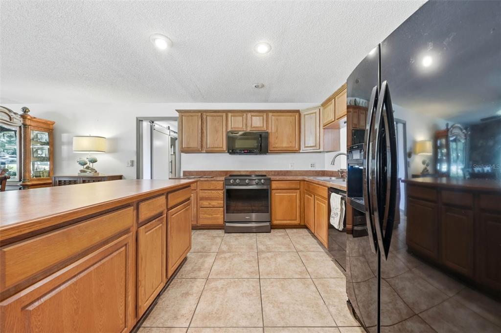 A living room and kitchen area with tile flooring, wooden cabinets, and ceiling fans — 37237 GRAYS AIRPORT ROAD, LADY LAKE, FL