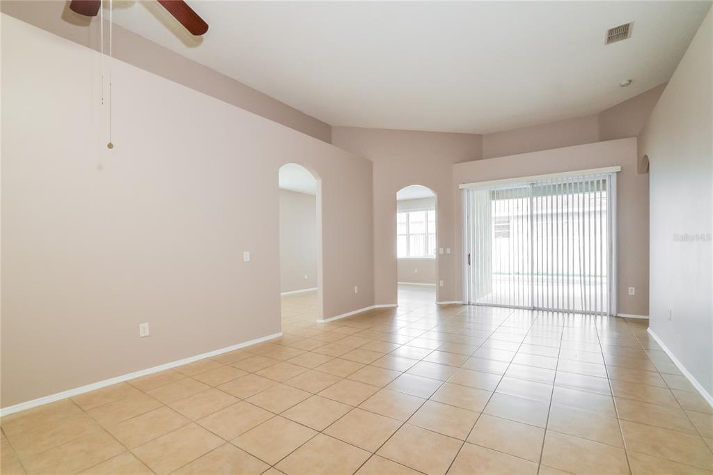 A spacious living room with beige tile flooring, vaulted ceilings, and sliding glass patio doors — 1671 ISLEBROOK DRIVE, ORLANDO, FL