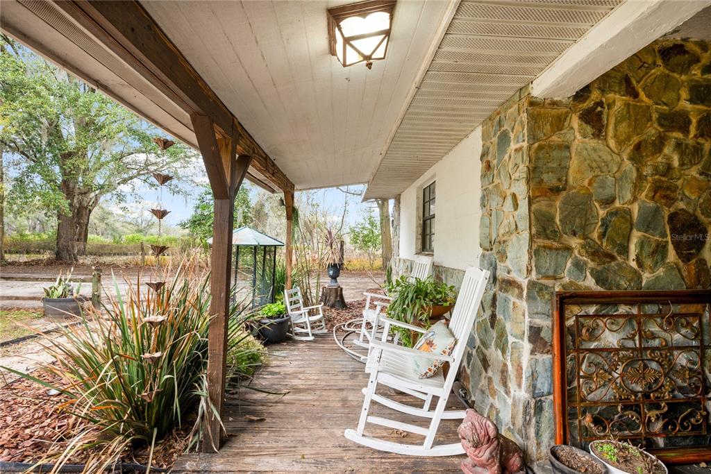 A covered wooden porch features white rocking chairs and a stone exterior wall — 12237 CR 727, WEBSTER, FL