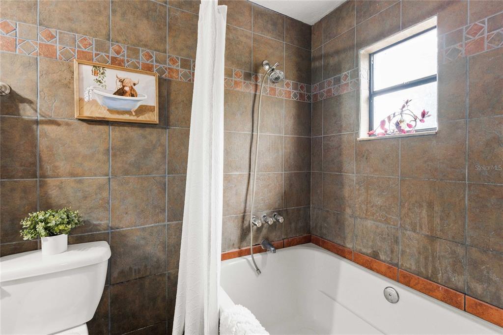 A bathroom features brown tiled walls, a white bathtub with a showerhead, and a toilet — 12237 CR 727, WEBSTER, FL