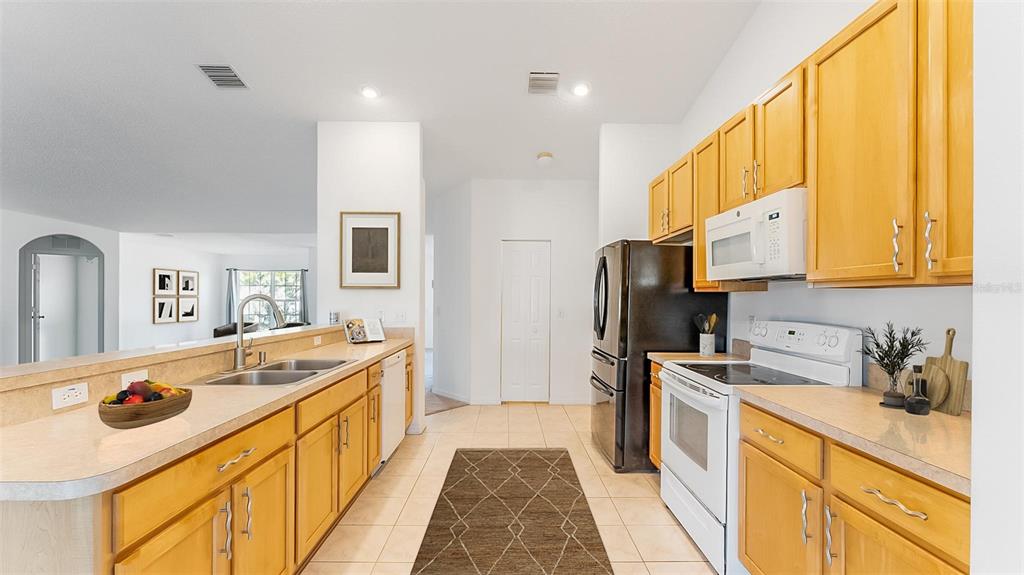 A kitchen with light wood cabinets, white appliances, and a breakfast bar overlooking a room — 8 WHITE HURST LANE, PALM COAST, FL
